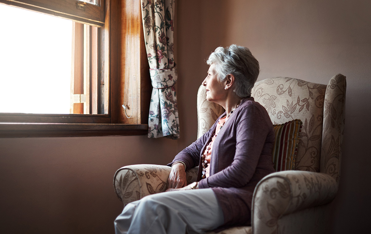Senior woman sitting alone in a chair and gazing out her window