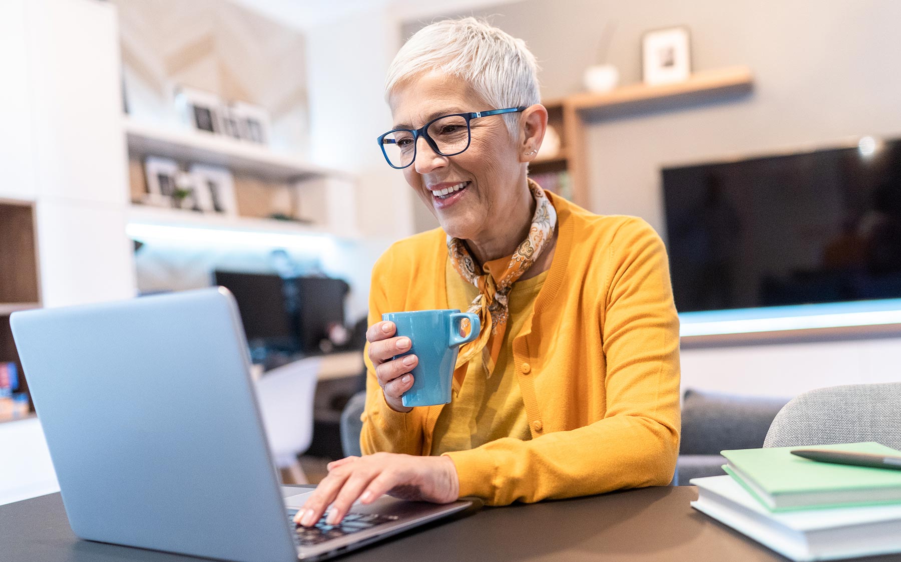 senior woman holding a coffee mug smiling and looking at her laptop