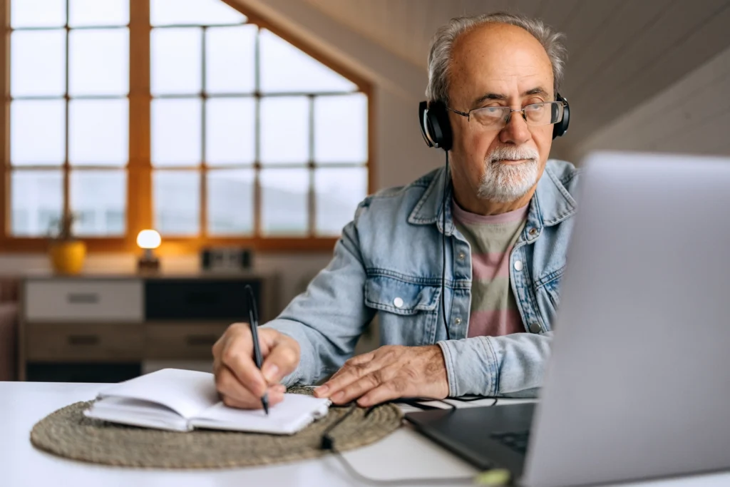 A man taking notes during an online lifelong learning program for seniors in his home at Whitestone, a senior living community in Greensboro, SC.
