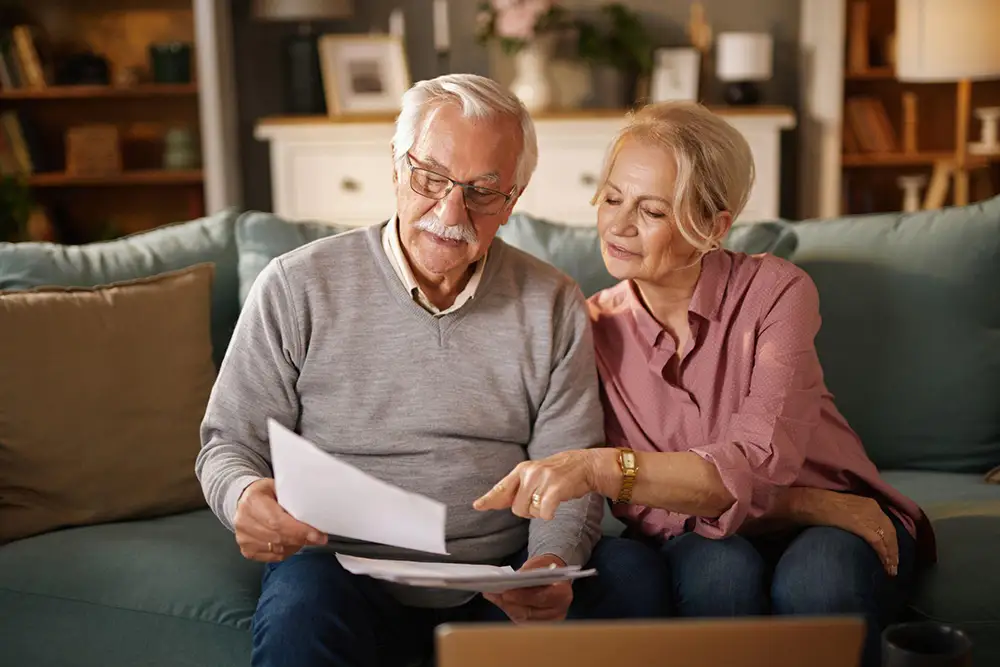 A senior couple sitting on a living room sofa, carefully reviewing financial or legal documents together for estate planning for seniors.
